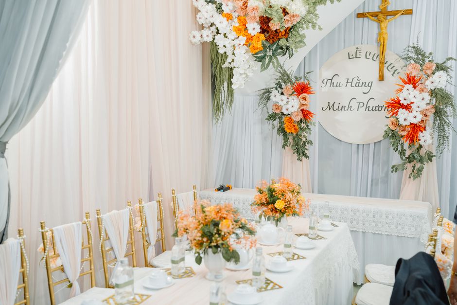 A wedding ceremony setup featuring a floral arrangement with a variety of fresh flowers, including white and orange chrysanthemums, peach roses, and greenery, integrated into a large, cascading bouque